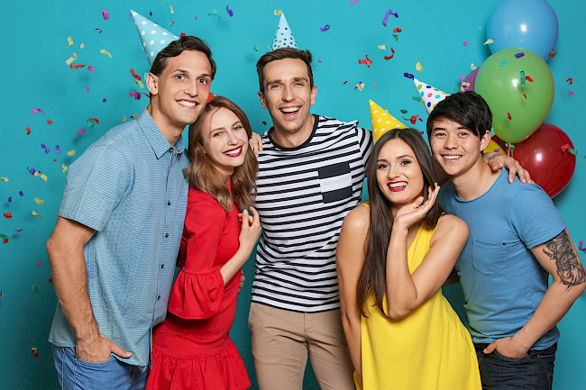 Freunde mit Partyhüten feiern Geburtstag mit Luftballons und Konfetti