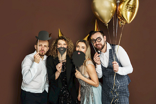 Gruppe mit goldenen Luftballons und Fotorequisiten posiert für ein Erinnerungsfoto