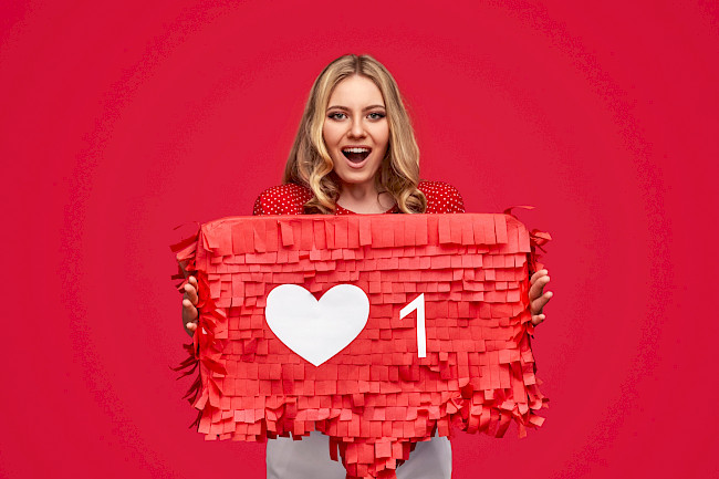 Frau hält eine rote Like-Requisite mit Herz in die Kamera