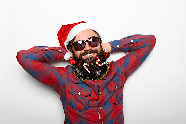 Mann mit Weihnachtsmütze und geschmücktem Bart posiert entspannt
