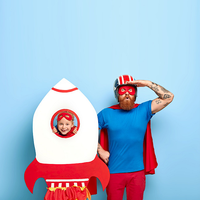 Papa und Kind posieren als Superhelden mit Raketen-Requisite
