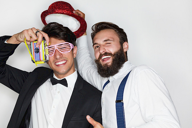 Hochzeitsgäste im Anzug mit Partybrille, Hut und Kamera haben Spaß