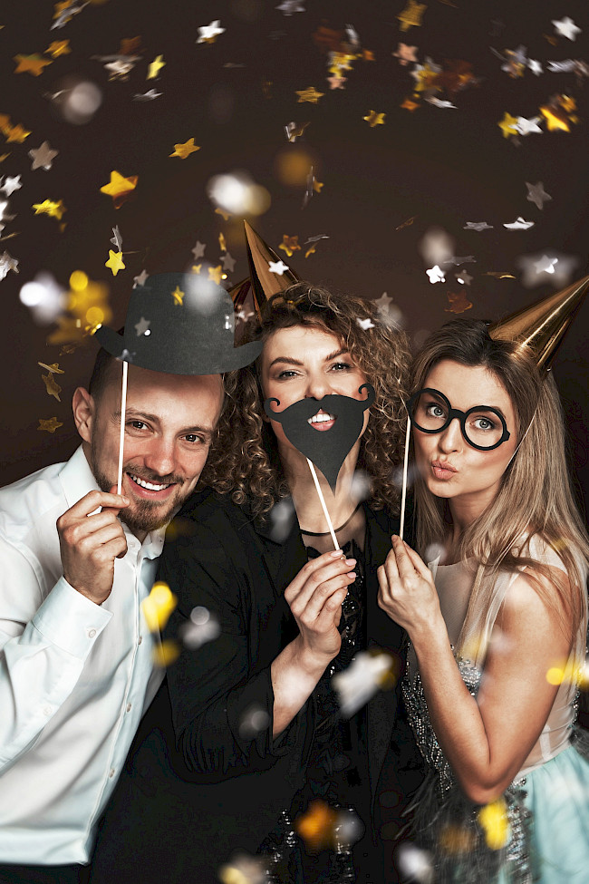 Eventgäste mit Partyhüten und Fotorequisiten im Konfettiregen