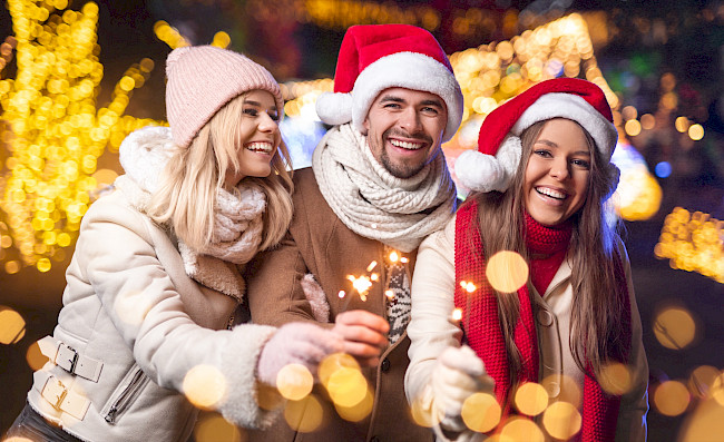 Freunde mit Weihnachtsmützen und Wunderkerzen feiern im Freien