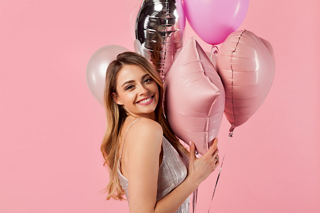 Frau mit rosa Luftballons lacht vor rosa Hintergrund