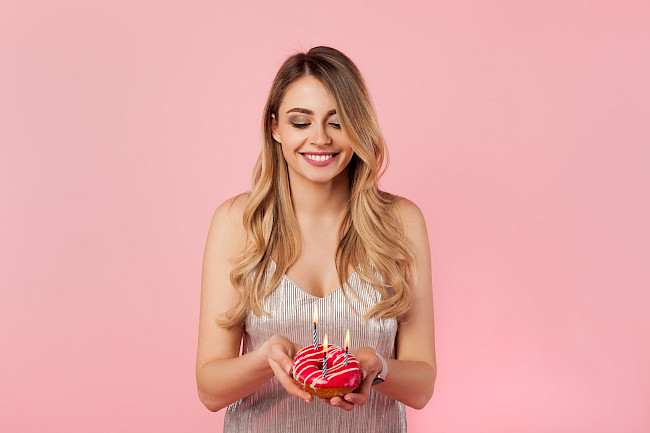 Frau hält zum Geburtstag einen Donut mit Kerzen