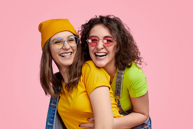 Zwei Freundinnen lachen gemeinsam vor rosa Hintergrund